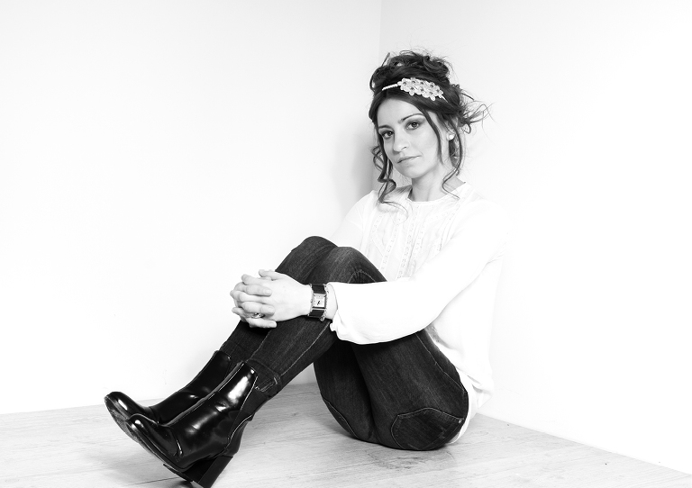 Retrato moda en blanco y negro de plano general realizado a Sharai que está sentada con las manos entrelazadas en las piernas  y viste un pantalón vaquero con camisola blanca y un tocado en el pelo realizado por Leyre Benito, la Fotografía realizada por Alberto Cossío Fotografía de moda en donostia